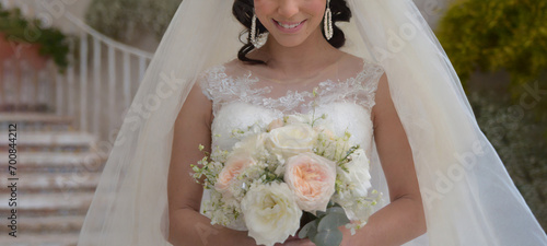 Beautiful woman dressed as a bride, with a white dress and a bouquet of flowers. Pretty white woman with black hair. Girl about to get married or recently married. photo