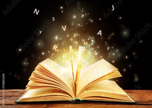 Cuadro en lienzo Open book with magic light and glowing letters flying out of it on wooden table