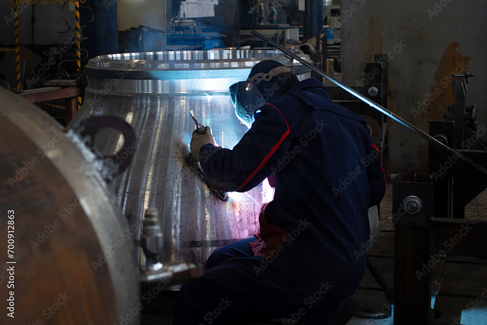 A welder works with a large metal structure at a mechanical engineering plant.