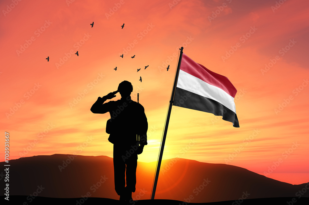 Silhouette of a soldier with the Yemen flag stands against the background of a sunset or sunrise. Concept of national holidays. Commemoration Day.