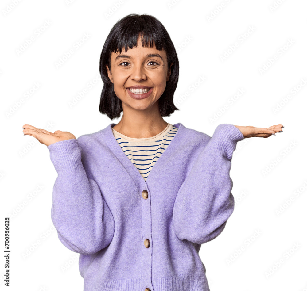 Young Hispanic woman with short black hair in studio makes scale with arms, feels happy and confident. Young Hispanic woman with short black hair in studio makes scale with arms, feels happy and confident.