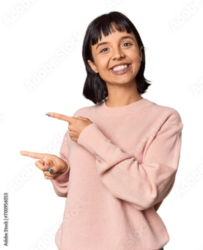 Young Hispanic woman with short black hair in studio excited pointing with forefingers away.
