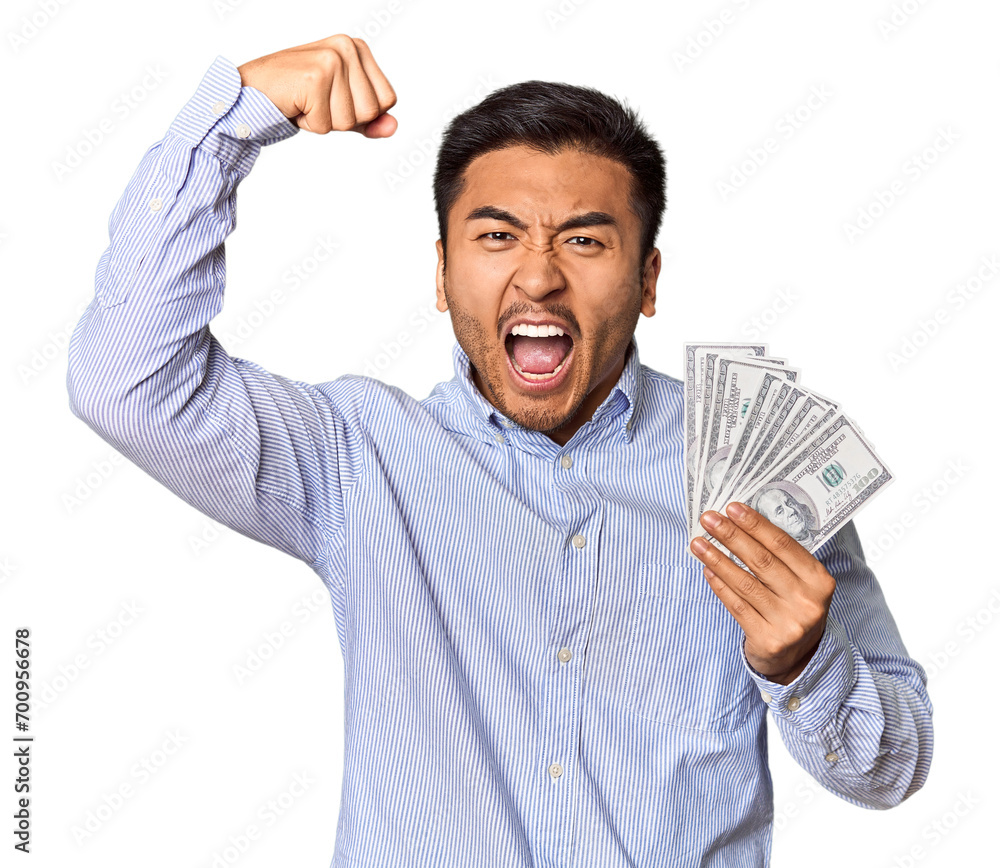 Young Chinese man holding dollar bills in studio raising fist after a victory, winner concept. Young Chinese man holding dollar bills in studio raising fist after a victory, winner concept.