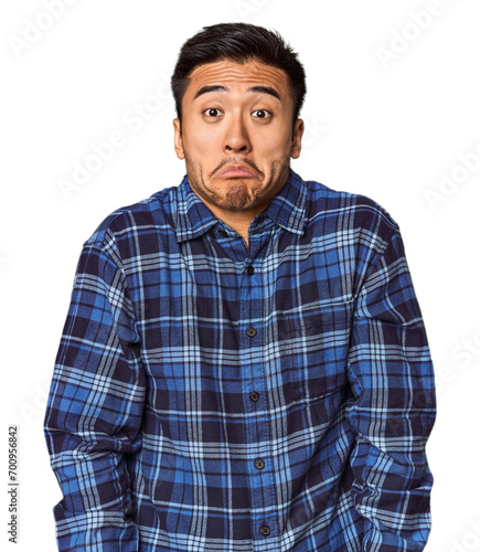 Young Chinese man in studio background shrugs shoulders and open eyes confused.