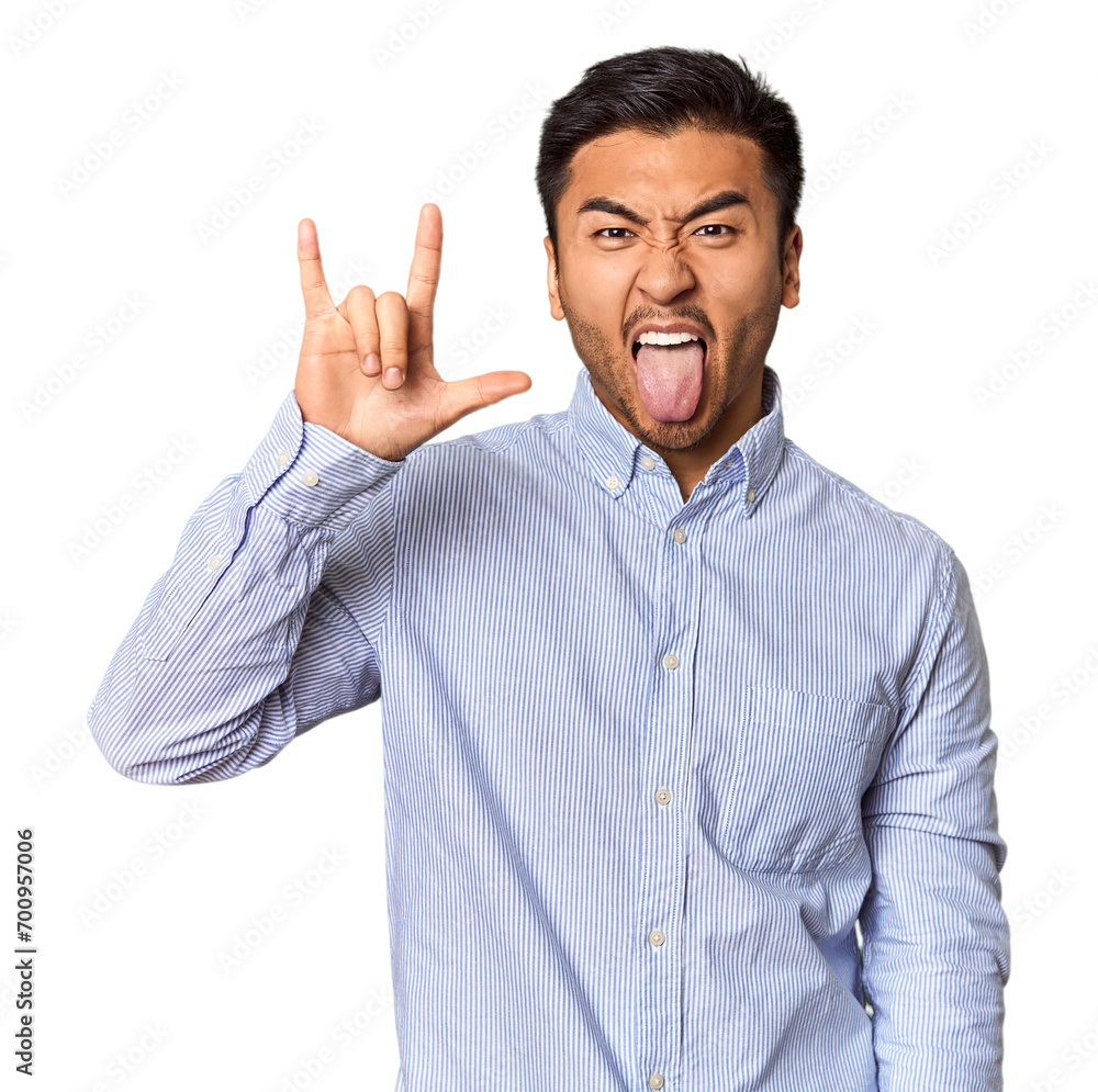 Young Chinese man in studio background showing a horns gesture as a revolution concept. Young Chinese man in studio background showing a horns gesture as a revolution concept.