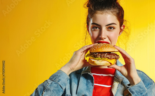 A young girl laughing and holding a fresh crispy hamburger in her hand on a yellow background