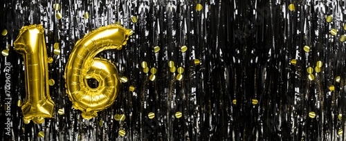 Gold foil balloon number number 16 on a background of black tinsel decoration. Birthday greeting card, inscription sixteen. Anniversary event. Banner. photo