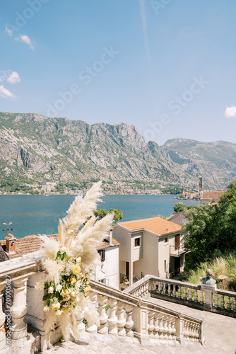 Bouquet of flowers stands on the steps near the balustrade overlooking the red roofs of houses and the sea