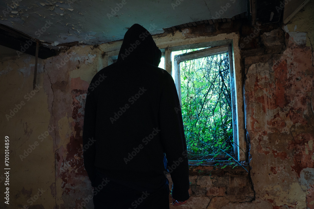 A horror concept of a scary hooded figure, back to camera. Silhouetted by a window in an abandoned house. With decaying walls. A horror concept of a scary hooded figure, back to camera. Silhouetted by a window in an abandoned house. With decaying walls.
