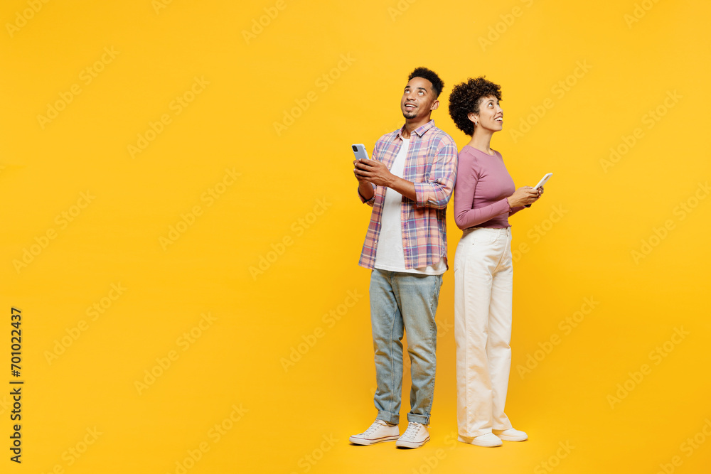 Full body young couple two friend family man woman of African American ethnicity in purple casual clothes together hold use mobile cell phone look overhead on area isolated on plain yellow background. - obrazy, fototapety, plakaty 