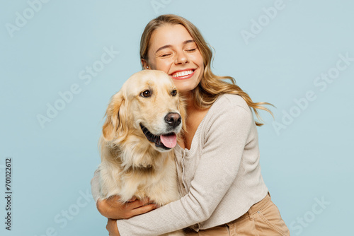 Young smiling happy cheerful owner woman with her best friend retriever wear casual clothes cuddle hug dog close eyes isolated on plain pastel light blue background studio Take care about pet concept