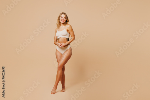 Full body smiling happy young nice lady woman with slim body perfect skin wear nude top bra lingerie stand looking aside on area isolated on plain pastel beige background. Lifestyle diet fit concept.