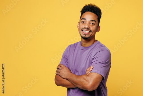 Side view young smiling happy man of African American ethnicity he wears purple t-shirt casual clothes hold hands crossed folded isolated on plain yellow background studio portrait. Lifestyle concept.