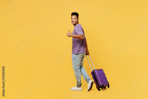 Traveler man wears summer casual clothes hold bag show thumb up walk isolated on plain yellow background studio. Tourist travel abroad in free spare time rest getaway. Air flight trip journey concept. #701024416
