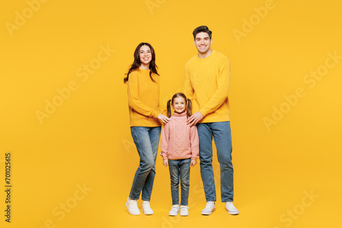 Full body young happy parents mom dad with child kid girl 7-8 years old wear pink sweater casual clothes put hand on little daughter look camera isolated on plain yellow background Family day concept photo
