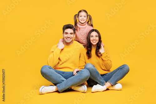 Full body young smiling happy fun parents mom dad with child kid girl 7-8 years old wearing pink sweater casual clothes sitting look camera hug isolated on plain yellow background. Family day concept.