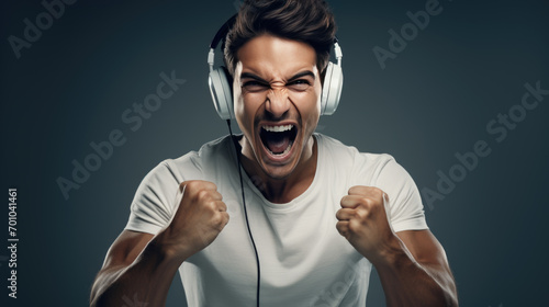 Man with white headphones on his ears, clenching his fists and yelling excitedly against a blue background.