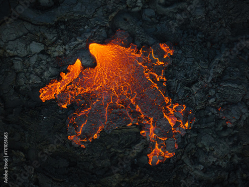 Obraz na plátně Unique view of molten lava flow burning and slowly moving down rugged volcanic rocks terrain, aerial close up shot