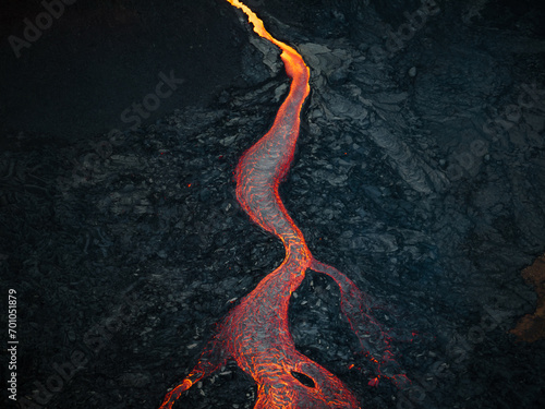 Fotografie Mesmerizing view of a lava flow, red hot molten liquid streaming over black solid volcanic rocks, aerial directly above shot