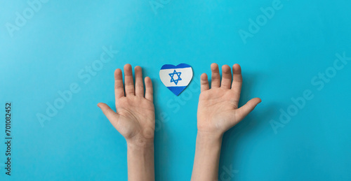 children of Israel with love for their native country. child's hands and a paper-cut drawn Israeli flag in the shape of a heart on a blue background. photo
