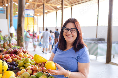 Photos A joyful and smiling brazilian mature woman at a market, holding two papayas, il