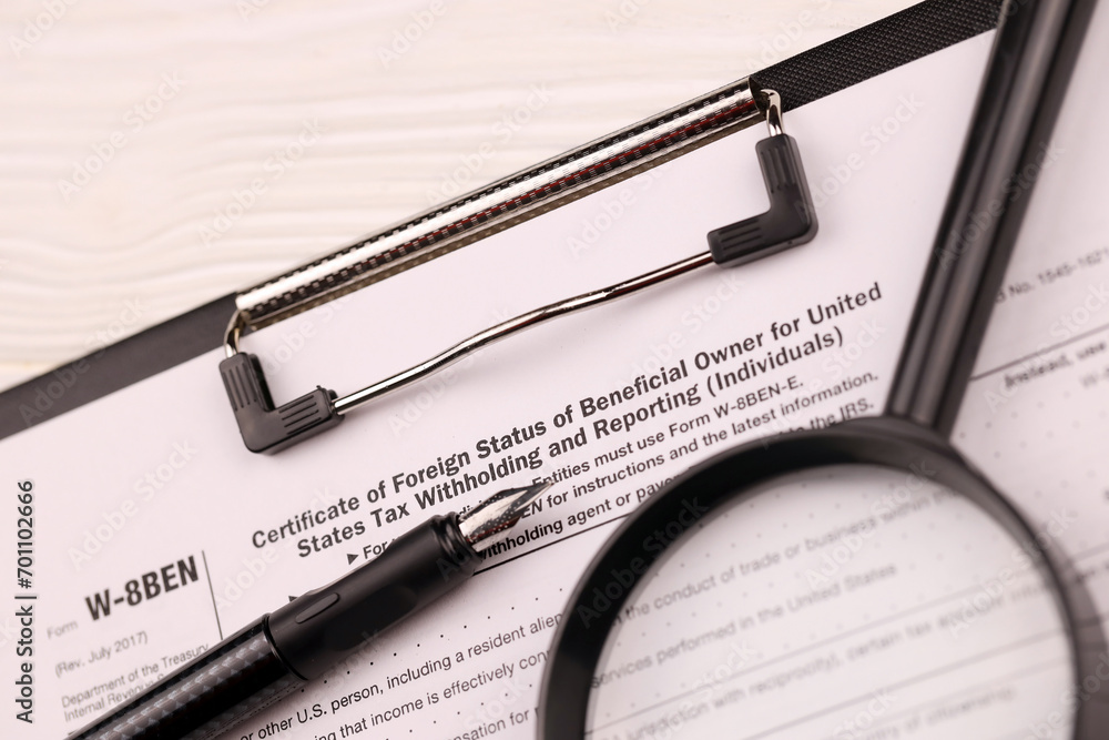 IRS Form W-8BEN Certificate of foreign status of beneficial owner for United States tax withholding and reporting blank on A4 tablet lies on office table with pen and magnifying glass close up