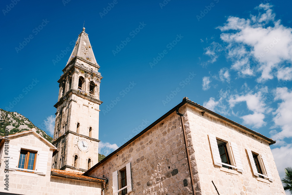 Old stone house with white shutters and an attic against the backdrop of the bell tower of the Church of St. Nicholas. Perast, Montenegro