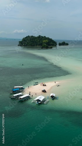 Boats floating over the turquoise water and ocean waves. Vanishing Island and Turtle Island in Barobo, Surigao del Sur. Philippines. Vertical view. photo