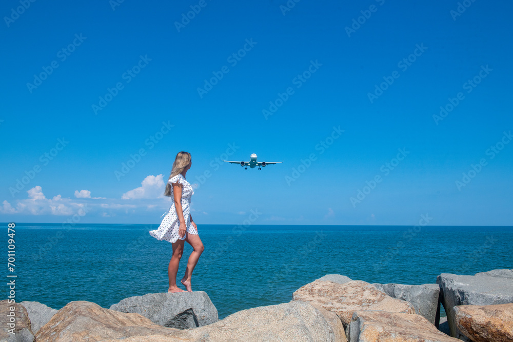 Coastal Magic: Girl in White Dress on Stones, Meeting a Plane by the Blue Sea Coastal Magic: Girl in White Dress on Stones, Meeting a Plane by the Blue Sea