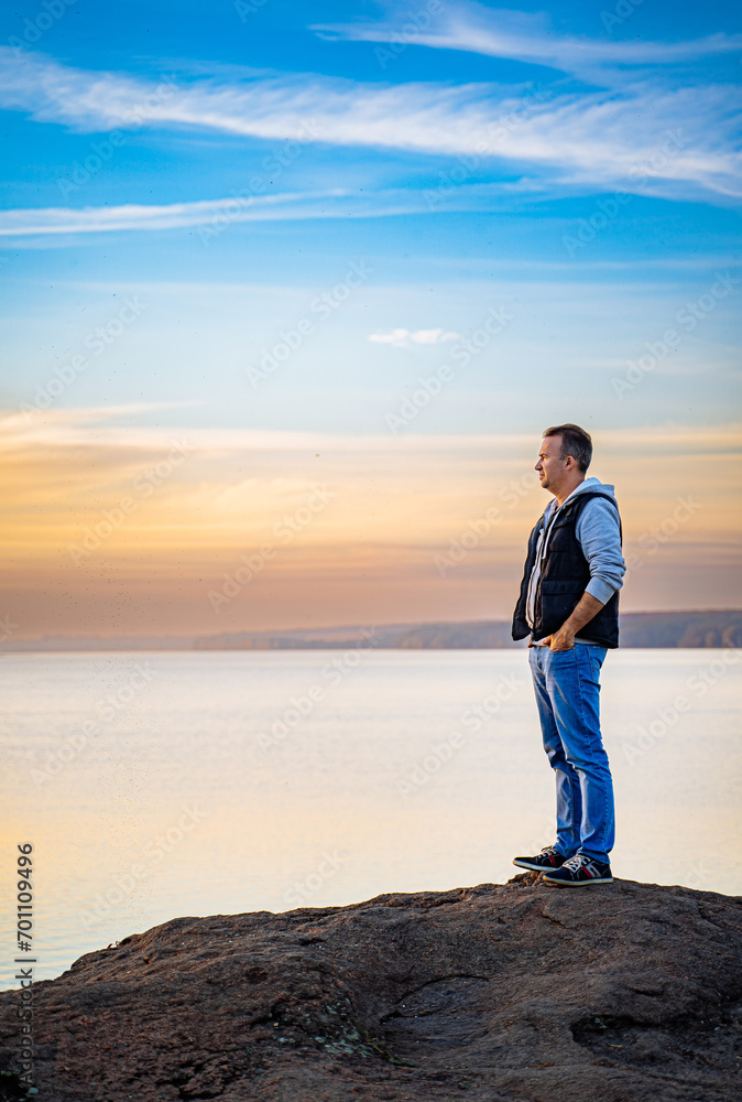 Man Enjoying Serene View From Rocky Outcrop. A man standing on top of a rock next to a body of water Man Enjoying Serene View From Rocky Outcrop. A man standing on top of a rock next to a body of water