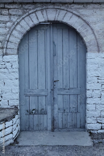 Old grayish-blue, double leaf, round arch wood door cut into a stone wall, old town upper part. Gjirokaster-Albania-187 photo