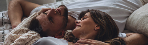 Banner relationships. Beautiful happy loving young couple relaxing in bed, looking at each other. Cozy home atmosphere, tenderness, closeness. Embracing, kissing. Lazy weekend, slow living concept
