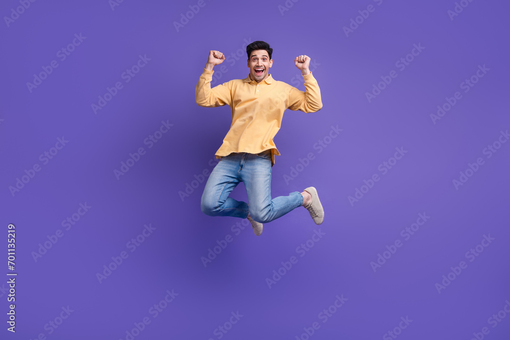 Obraz premium Full size photo of attractive young man jumping raise fists celebration dressed stylish yellow clothes isolated on purple color background