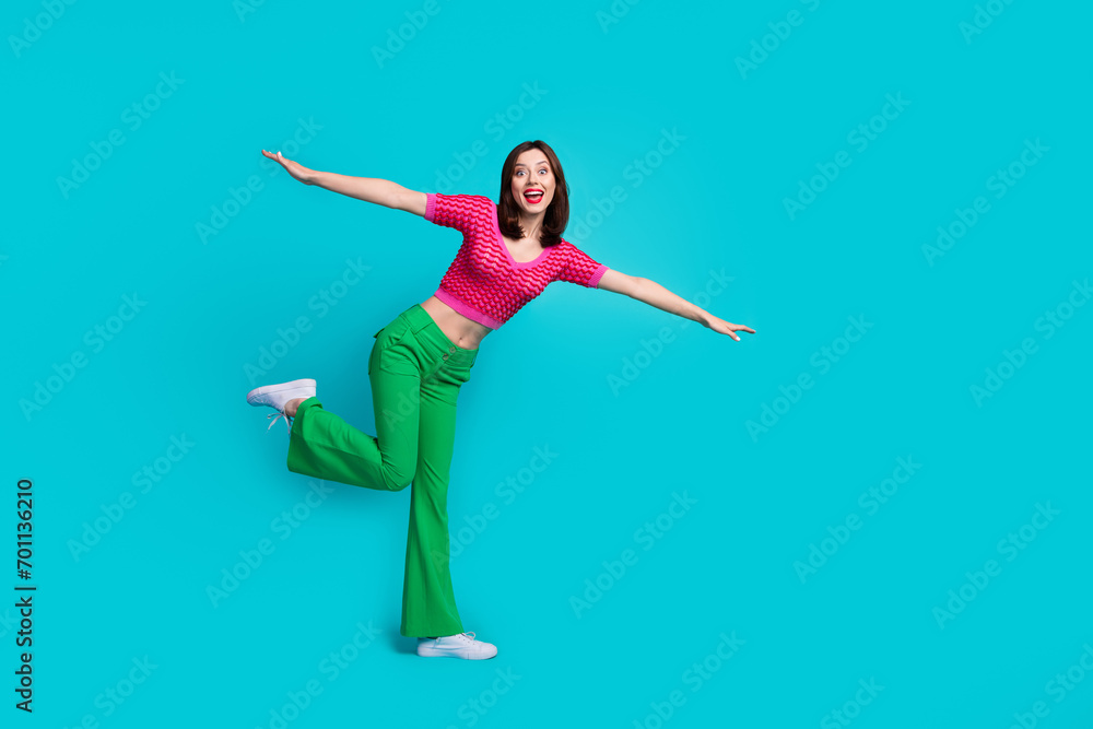 Full length photo of positive overjoyed woman dressed top green pants flying hold palms like wings isolated on blue color background Full length photo of positive overjoyed woman dressed top green pants flying hold palms like wings isolated on blue color background