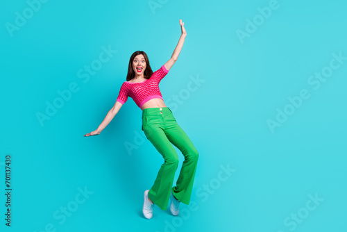 Full length photo of cute careless woman dressed pink top green retro pants stand on tiptoes falling isolated on blue color background
