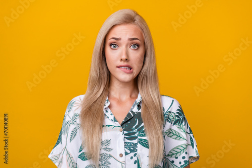 Photo of confused clueless pretty woman with straight hairdo dressed stylish print shirt biting lips isolated on yellow color background