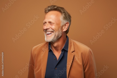 Portrait of happy mature man laughing and looking away on brown background