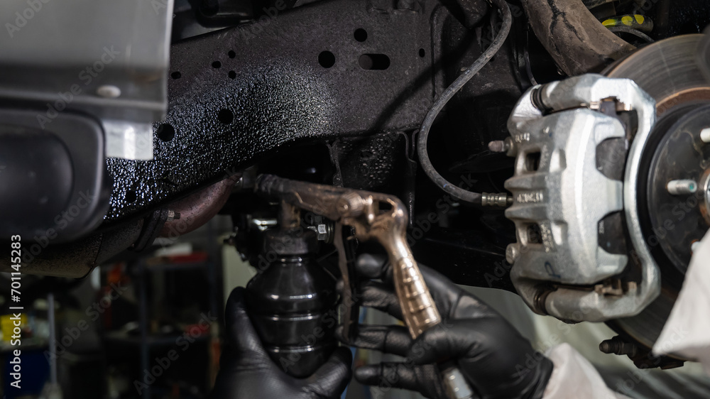 An auto mechanic applies anti-corrosion mastic to the underbody of a car. An auto mechanic applies anti-corrosion mastic to the underbody of a car.