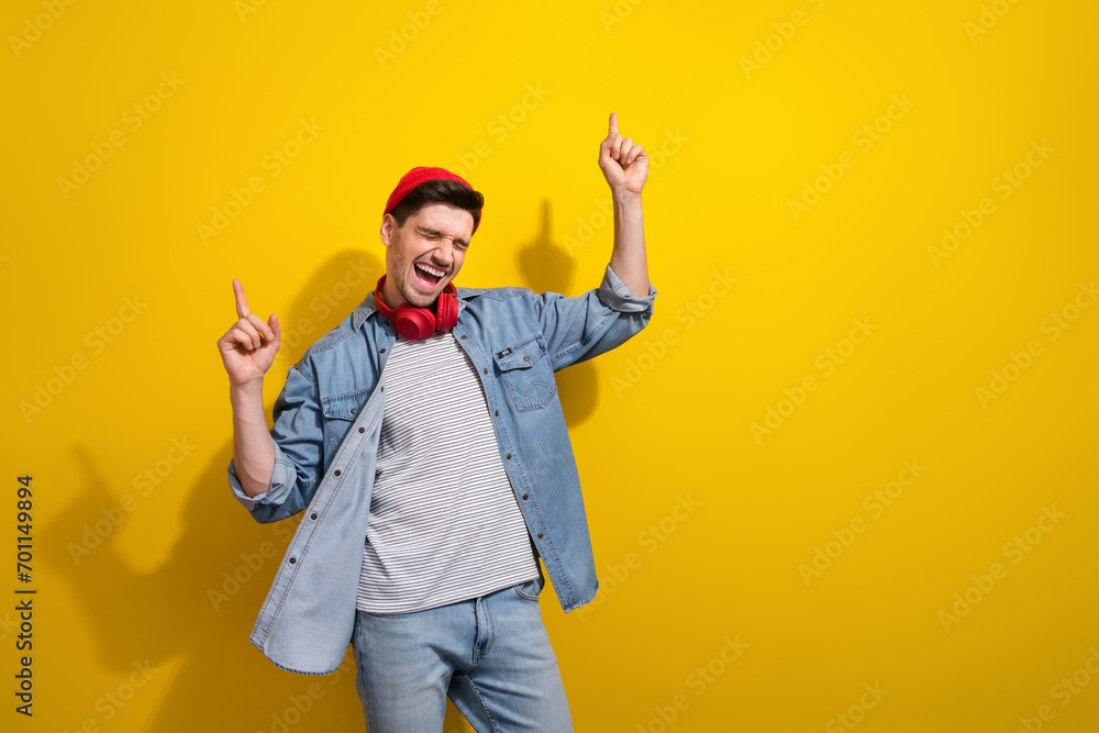 Photo of excited funky man dressed jeans shirt dancing pointing two fingers empty space isolated yellow color background