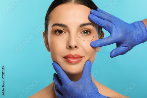 Doctor checking patient s face before cosmetic surgery operation on light blue background  closeup