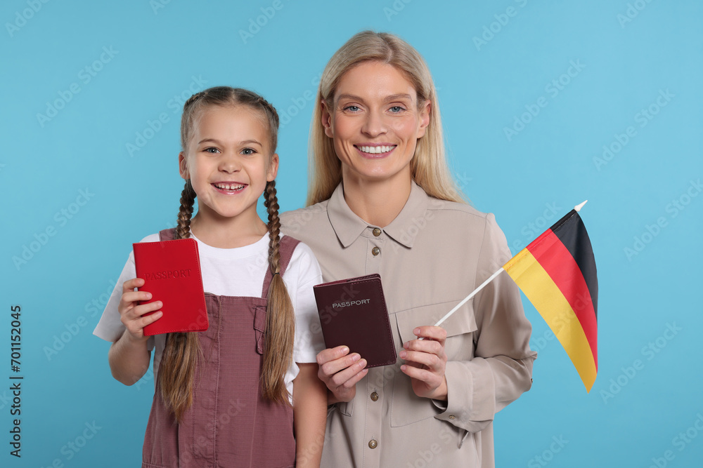 Immigration. Happy woman with her daughter holding passports and flag of Germany on light blue background Immigration. Happy woman with her daughter holding passports and flag of Germany on light blue background