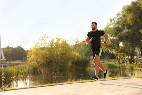 Fototapeta Naklejka Na Ścianę i Meble -  Young man running near pond in park. Space for text