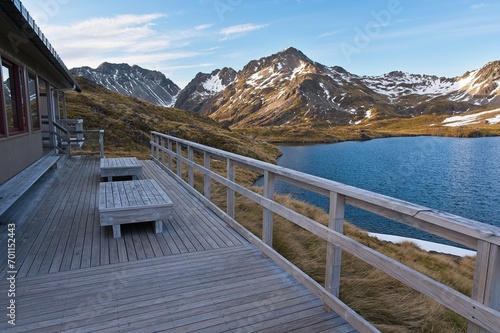 Lakeside Wooden Cabin: Rustic Hut Nestled by the Water with Snowy Mountain Backdrop.