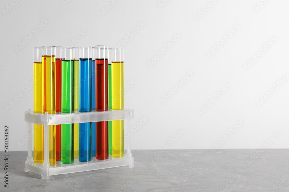 Test tubes with liquids in stand on grey table against white background, space for text Test tubes with liquids in stand on grey table against white background, space for text