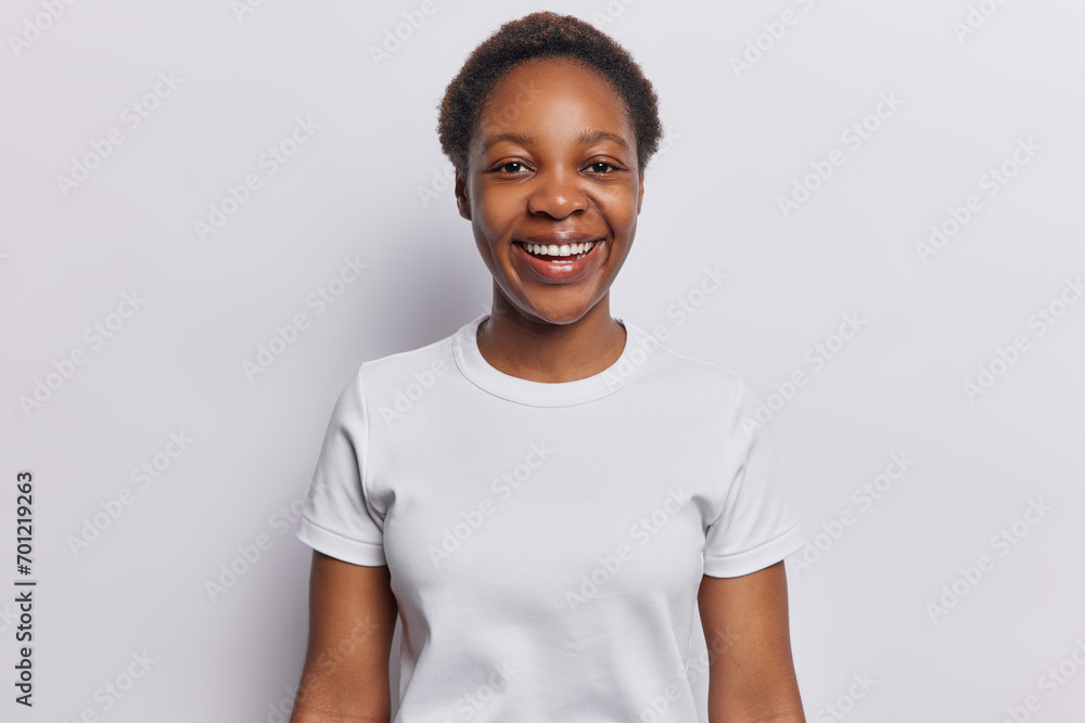 People positive emotions concept. Indoor shot of young happy smiling broadly African american female wearing casual clothes standing isolated on centre on white background keeping hands down People positive emotions concept. Indoor shot of young happy smiling broadly African american female wearing casual clothes standing isolated on centre on white background keeping hands down