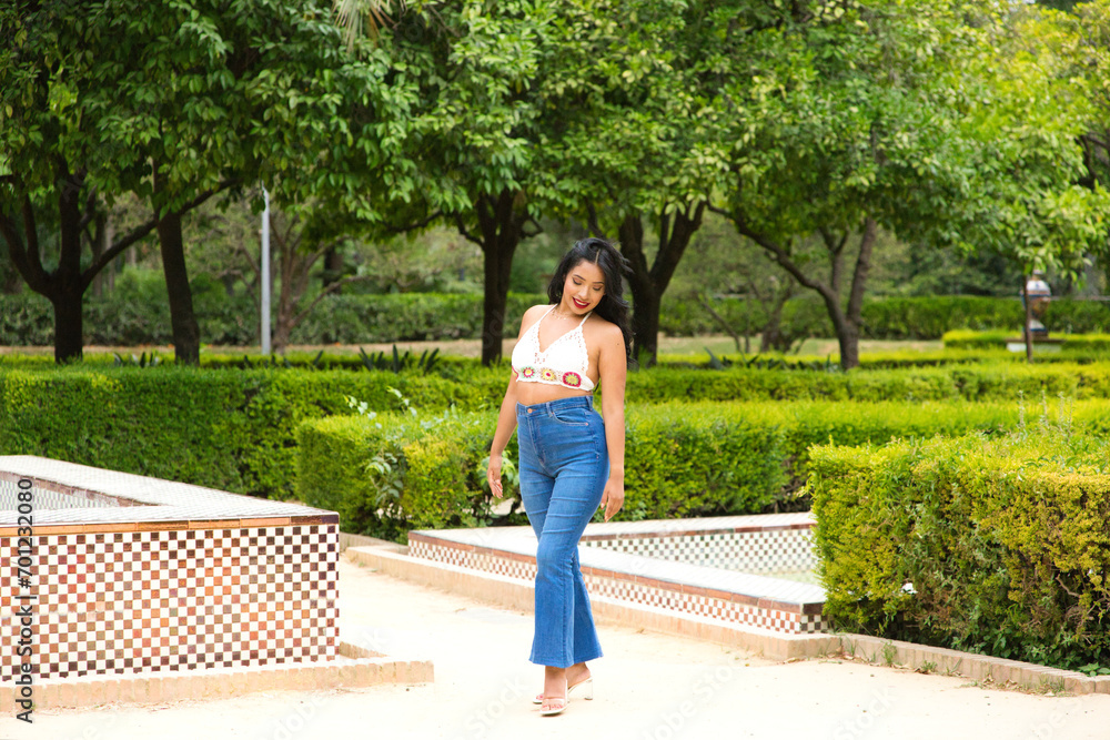 Naklejka premium Young and beautiful Latin woman from South America walks among the trees and vegetation of the park. The woman is smiling and happy and is posing for photos. Travel and holiday concept.