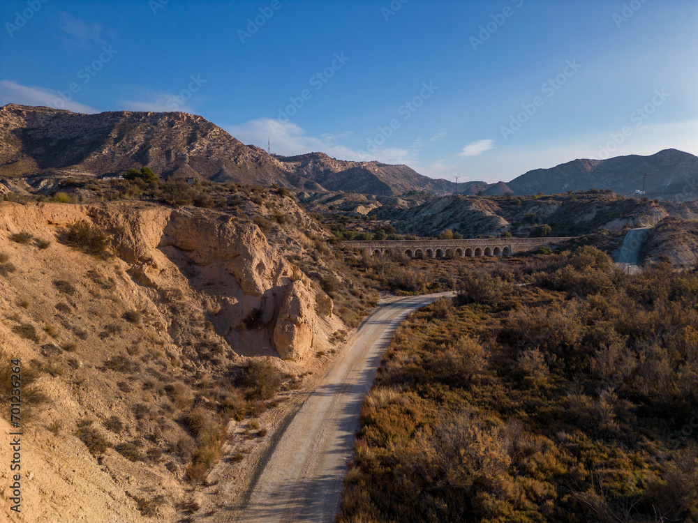 Dirt road in arid desert landscape with distant cliffs and morning sunlight, Elche, Alicante province, Spain - Stock photo Dirt road in arid desert landscape with distant cliffs and morning sunlight, Elche, Alicante province, Spain - Stock photo