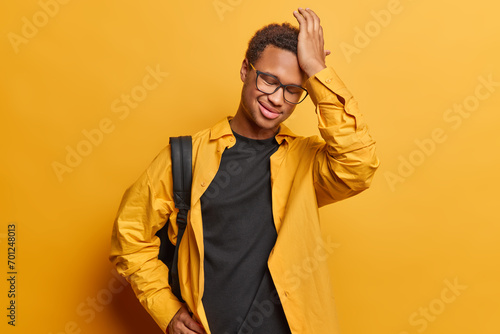 People positive emotions concept. Indoor portrait of satisfied smiling gently African american male wearing casual clothes standing in centre isolated on yellow background recalling something pleasant