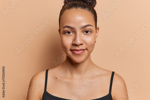 Portrait of healthy dark haired Latin woman with healthy clean skin has dimple on cheek dressed in casual t shirt isolated over brown background feels satisfied. Women and natural beauty concept photo
