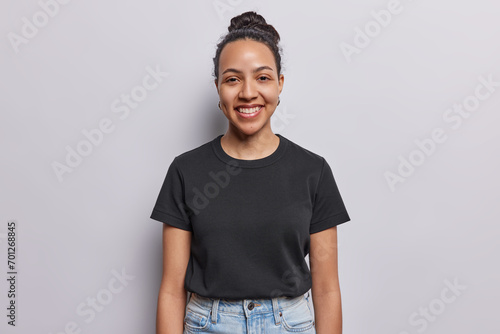 Waist up shot of cheerful Latin woman with combed hair and pleasant smile on face dressed in casual black t shirt annd jeans concentrated at camera isolated on white background. Happy face expressions